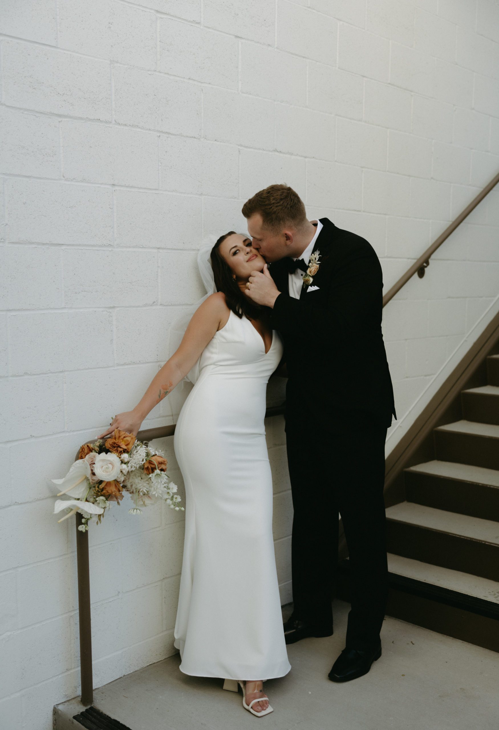 groom kissing bride cheek by staircase