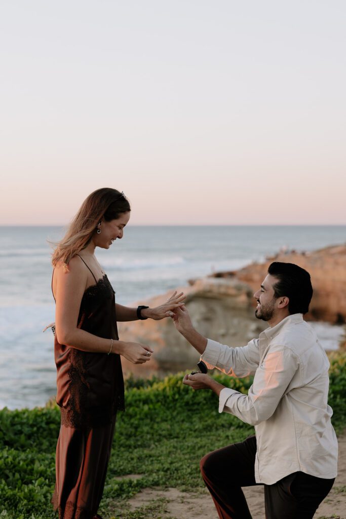 Emmanuel proposing to Camila with the ocean in the background at Sunset Cliffs proposal in San Diego