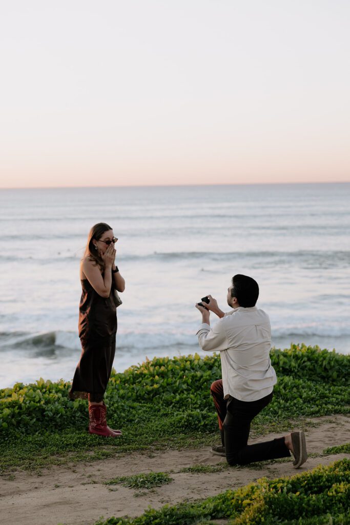 Emmanuel proposing to Camila with the ocean in the background at Sunset Cliffs proposal in San Diego