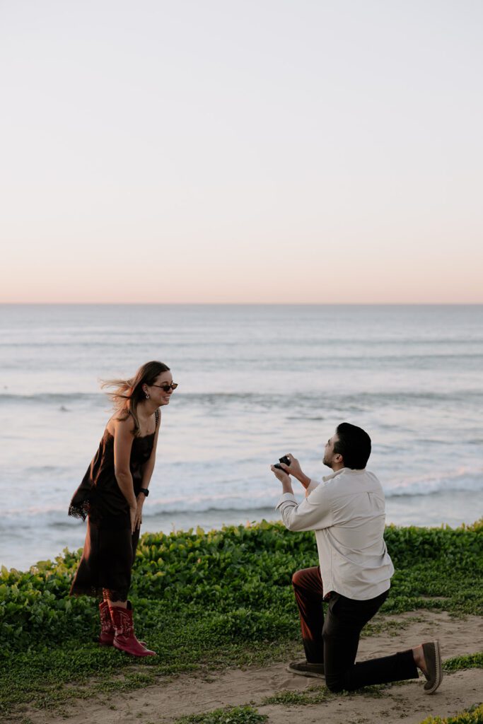 Emmanuel proposing to Camila with the ocean in the background at Sunset Cliffs proposal in San Diego
