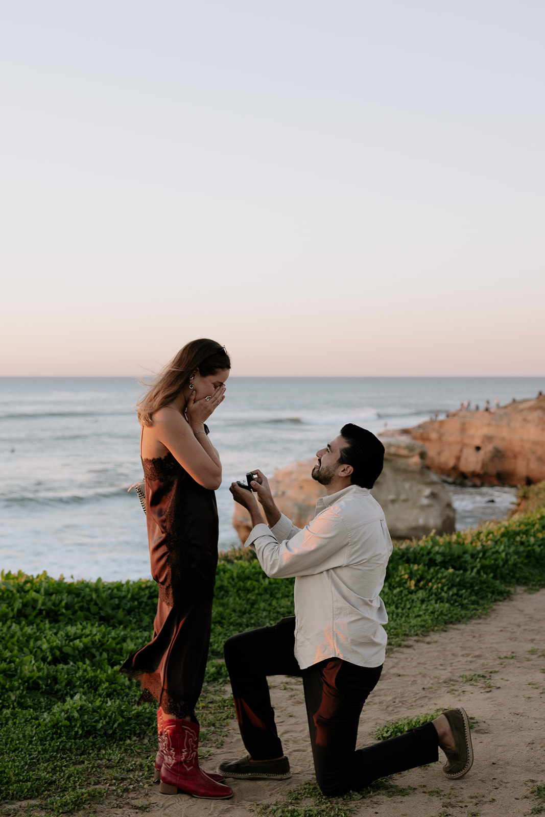 Emmanuel proposing to Camila with the ocean in the background at Sunset Cliffs proposal in San Diego